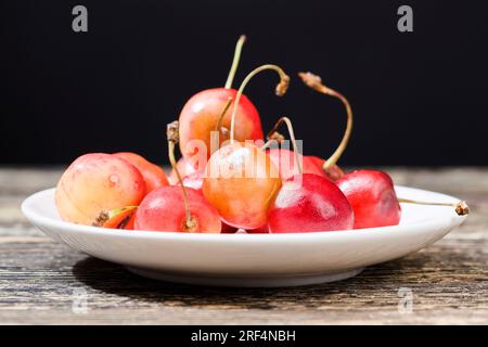 Verfaulte Kirschen auf einem Holztisch, ein paar Beeren, die bereits begonnen haben zu verrotten und mit Schimmel bedeckt, nicht essbar und gesundheitsgefährdend che Stockfoto