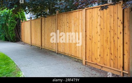 Schöner neuer Holzzaun um das Haus herum. Holzzaun mit grünem Rasen an einem sonnigen Sommertag. Straßenfoto, niemand, selektiver Fokus Stockfoto