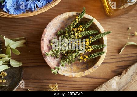 Getrocknete Agrarblumen in einer Schüssel auf einem Tisch, mit Zichorie- und Lindenblüten im Hintergrund Stockfoto