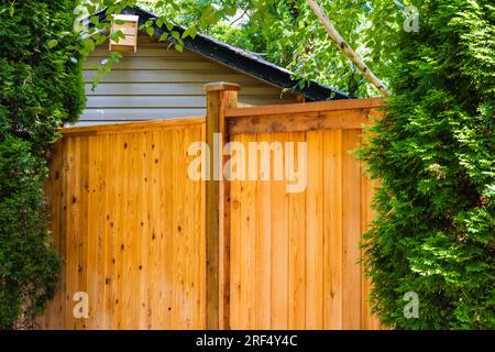 Schöner neuer Holzzaun um das Haus herum. Neuer Holzzaun mit Bäumen. Solider Zedernzaun. Straßenfoto, niemand, selektiver Fokus. Stockfoto