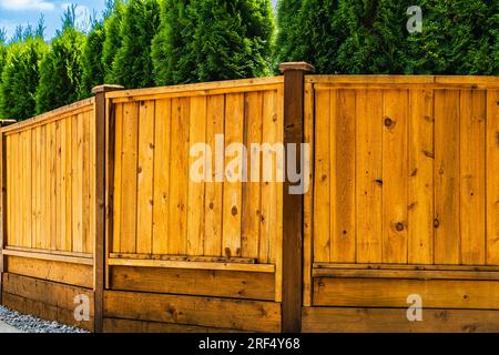 Schöner neuer Holzzaun um das Haus herum. Neuer Holzzaun mit Bäumen. Solider Zedernzaun. Straßenfoto, niemand, selektiver Fokus. Stockfoto