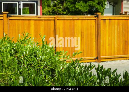 Schöner neuer Holzzaun um das Haus herum. Neuer Holzzaun mit Bäumen. Solider Zedernzaun. Straßenfoto, niemand, selektiver Fokus. Stockfoto