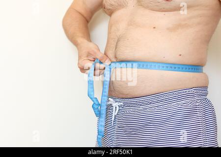Ein Mann misst seinen fetten Bauch mit Maßband. Konzept der Gewichtsabnahme, Gesundheitsprobleme von übergewichtigen Menschen. Schlechte Ernährung und sitzender Lebensstil. Inkr Stockfoto