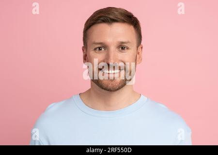 Porträt eines weißen, bärtigen, gutaussehenden Mannes, der auf pinkfarbenen Studiohintergrund vor der Kamera lächelt. Stockfoto