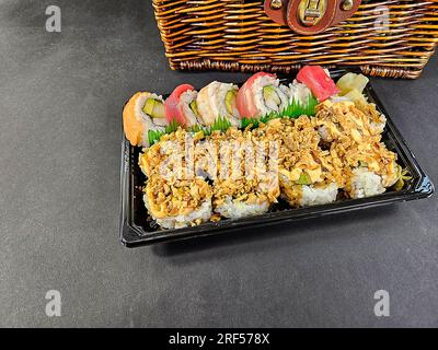 Frische Sushi-Brötchen auf einer schwarzen Kunststoffschale mit braunem Korb aus Korb Stockfoto