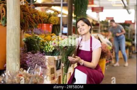 Asiatische Blumenmeisterin, die auf dem Blumenmarkt ein Blumenstrauß mit blühenden Ammi anbietet Stockfoto