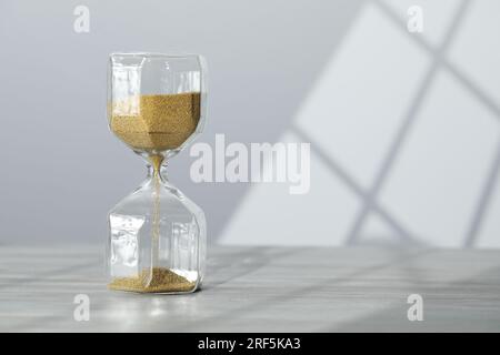 Sanduhr mit fließendem goldenen Sand auf dem Tisch an der weißen Wand, Platz für Text Stockfoto