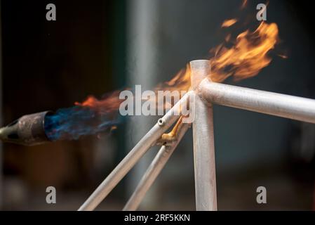 Manuelle Fahrradrenovierungsarbeiten, Lackentfernung durch Brennerfeuer, um die Farbe eines Fahrradrahmens zu ändern. Nahaufnahme, keine Menschen. Stockfoto