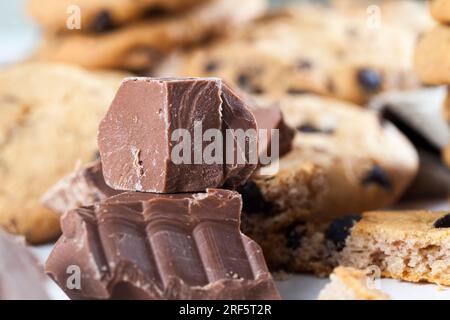 Große Stücke Milchschokolade auf dem Tisch, zerbrochene Schokolade und Weizenkekse mit Schokoladentropfen, Fast Food-Artikel, sehr kalorienreiches Kakaopulver Stockfoto