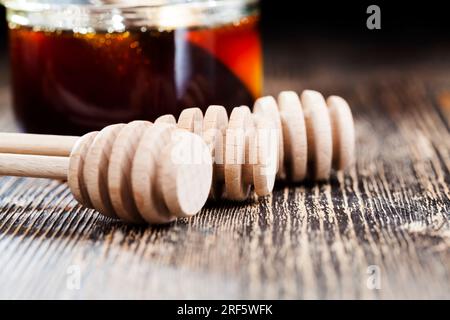 In Honig getaucht, der speziell aus Holz hergestellt wurde, ein hausgemachter Rohlöffel, süßer Bienenhonig und drei Holzlöffel, mit denen Sie Honig wi umfüllen und eingießen können Stockfoto