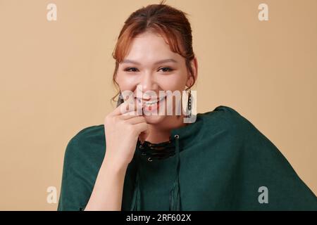 Porträt einer verspielten jungen asiatischen Transgender-Frau, die beim Lächeln vor der Kamera Lippen berührt Stockfoto