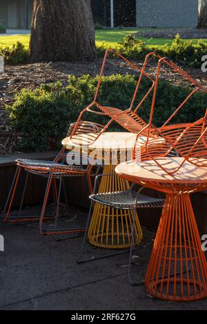 Stühle mit Drahtrahmen in leuchtendem Gelb und Orange sind ordentlich auf einem Tisch gestapelt und warten darauf, dass der Veranstaltungsort wieder geöffnet wird. Stockfoto