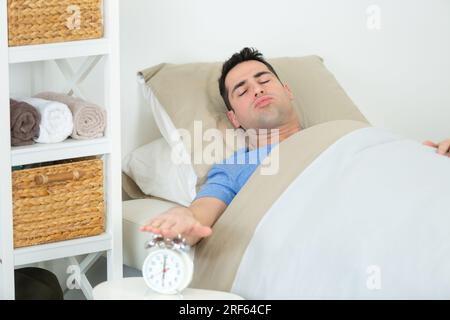 Fröhliches Aufwachen eines glücklichen Mannes, der den Wecker stoppt Stockfoto