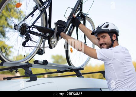 Radfahrer im Helm installiert sein Fahrrad auf dem Dach des Autos Stockfoto