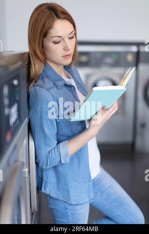 Junge Frau, die ein Buch im Waschsalon liest Stockfoto