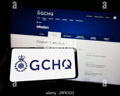 Person, die ein Smartphone mit dem Logo der Government Communications Headquarters (GCHQ) auf dem Bildschirm vor der Website hält. Konzentrieren Sie sich auf das Display des Telefons. Stockfoto