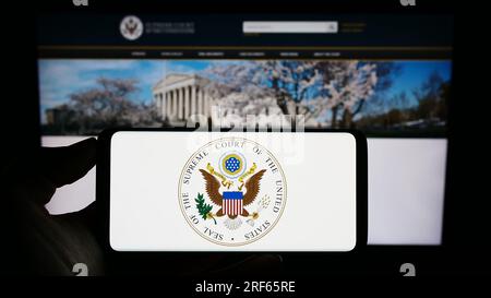 Person, die ein Mobiltelefon mit dem Siegel der USA hält Supreme Court (SCOTUS) auf dem Bildschirm vor der Webseite. Konzentrieren Sie sich auf das Display des Telefons. Stockfoto