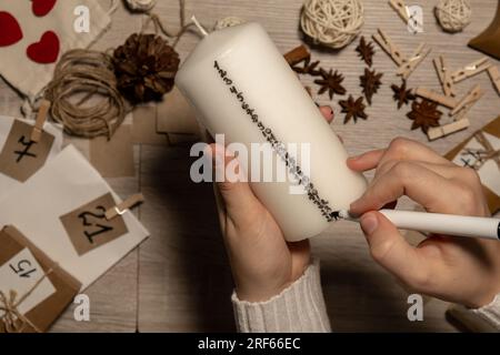 Eine nicht erkennbare junge Frau malt Zahlen auf Kerzen. Frau macht hausgemachte Adventskalender mit eigenen Händen gemacht Schritt für Schritt selbstgemachtes Kunsthandwerk Machen Sie es selbst. Vorbereitung auf das weihnachtskonzept. Saisonale Aktivitäten für Kinder, Familienurlaub im Winter. Umweltfreundlich Geschenke. Öffnen Sie das Paket jeden Tag Stockfoto