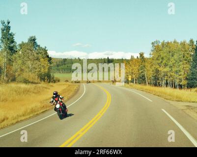 Blick von einem fahrenden Auto mit Blick auf ein Motorrad, das in der Sommersaison auf der Autobahn in Turner Valley, Alberta, Kanada fährt. Stockfoto