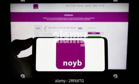 Person, die ein Mobiltelefon mit dem Logo von NOYB – European Center for Digital Rights (Europäisches Zentrum für digitale Rechte) auf dem Bildschirm vor der Webseite hält. Konzentrieren Sie sich auf das Display des Telefons. Stockfoto