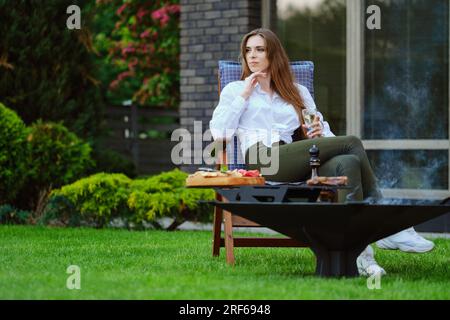 Eine wunderschöne junge Frau sitzt auf einem Klappstuhl im Garten und schaut zur Seite Stockfoto