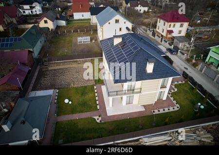 Draufsicht über das Haus mit Photovoltaik-Solarpaneelen auf dem Dach, umgeben von Hof-, Straßen- und Wohngebäuden. Haus mit Solarmodulen zur Stromerzeugung durch Photovoltaik. Stockfoto