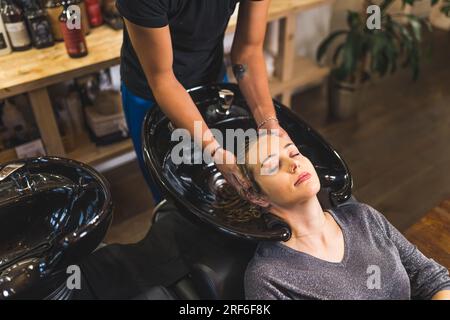 Eine entspannte Kundin, die ihr Haar von einem Friseur an einem Waschbecken in einem Friseurladen schamponieren ließ. Hochwertiges Foto Stockfoto