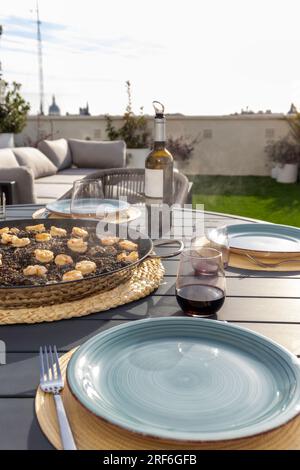 Schwarzer Reis mit Tintenfisch und Garnelen in einer Paella-Pfanne. Serviert mit Rotwein auf der Terrasse Stockfoto