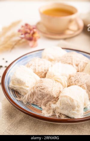 Traditionelle arabische Süßigkeiten Pishmanie und eine Tasse grüner Tee auf weißem Holzhintergrund und Leinentextilien. Seitenansicht, Nahaufnahme, selektiver Fokus. Stockfoto