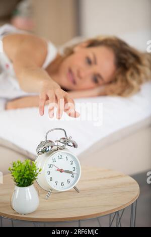 Glückliche junge Frau stellt den Wecker aus Stockfoto