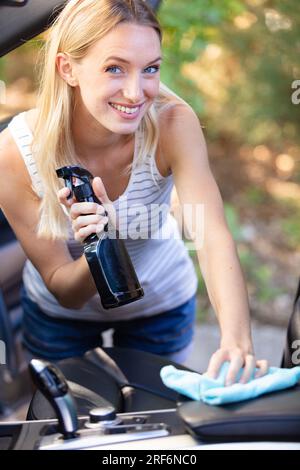 Glückliche junge Frau, die ihr Auto draußen putzt Stockfoto