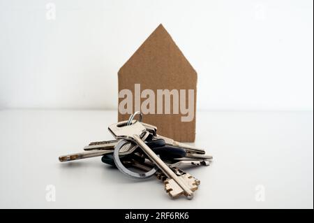 Ein Haufen Schlüssel vor dem Papierhaus. Hypotheken, Wohnungen, Finanzen, Immobilien, Häuser verkaufen, Verkauf Stockfoto