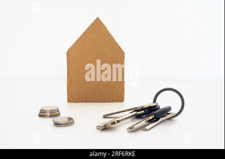 Papphaus mit einem Haufen Schlüssel und Münzen vorne. Hypotheken, Wohnungen, Finanzen, Immobilien, Häuser verkaufen, Verkauf Stockfoto
