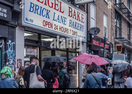 Touristen und Londoner stehen im Regen vor der Brick Lane Bakery für ihre berühmten Bagels. Stockfoto