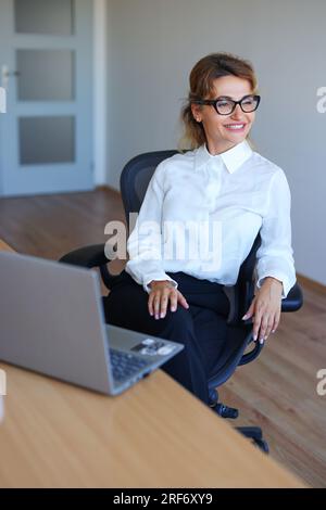 Porträt von fröhlichen Geschäftsfrau sitzt am Tisch im Büro Stockfoto