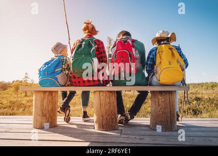 Mutter und Vater mit zwei Söhnen, die nach dem Wandern auf der Bank sitzen und sich entspannen. Stockfoto