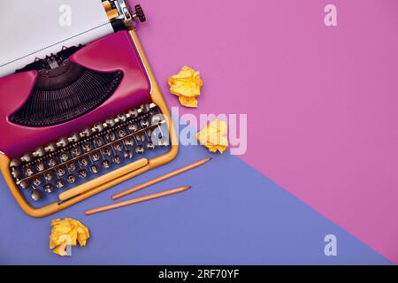 Werbetexter. Klassische Schreibmaschine, zerknitterte Papierkugeln und Bleistifte auf farbigem Hintergrund, Draufsicht. Platz für Text Stockfoto