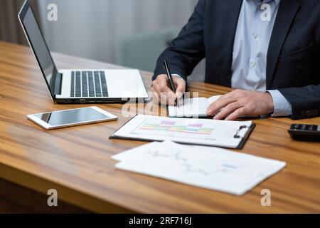 Die Hände des Geschäftsmanns schließen sich, der Mann am Tisch arbeitet mit Dokumenten und Papierverträgen. Stockfoto