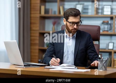 Seriöser Geschäftsmann hinter Papierarbeit, erfahrener Chefboss, der konzentriert im Büro am Tisch sitzt, Finanzier, Investor, unterzeichnet Vertrag. Stockfoto