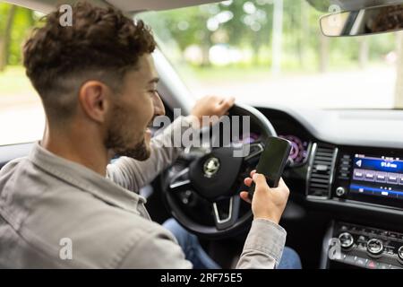 Ein Mann benutzt im Auto ein Handy und verschwimmt die schöne grüne Straße als Hintergrund. Stockfoto