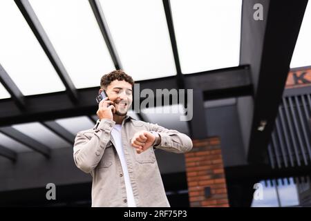 Beeilt euch! Porträt eines verantwortungsbewussten, attraktiven Mannes mit moderner Frisur, der ein wichtiges Gespräch mit einem Smartphone führt und auf eine Luxusuhr am Handgelenk-iso schaut Stockfoto