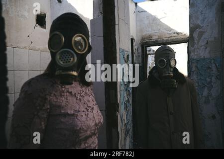 Die Frau in einer Gasmaske, die vor einem Mann in einem zerstörten Gebäude bleibt, gut für den Bucheinband Stockfoto