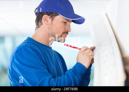 Junger Bauarbeiter in einem Schutzhelm, der die Wand misst Stockfoto