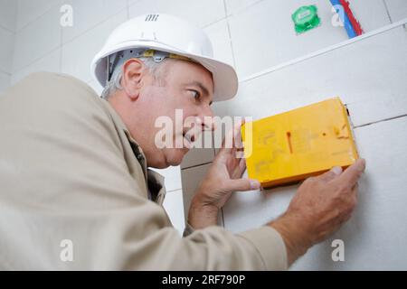 Der Elektriker installiert eine Kabelbox in einer neuen Wohnung Stockfoto