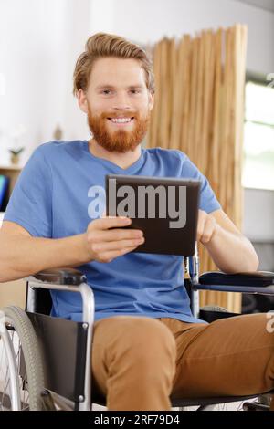 Glücklicher junger behinderter Mann, der es bemerkt, während er ein Tablet benutzt Stockfoto