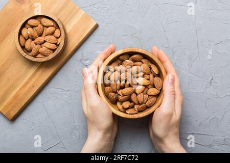 Frauenhände halten eine Holzschüssel mit Mandelnüssen. Gesundes Essen und Snack. Vegetarische Snacks mit verschiedenen Nüssen. Stockfoto