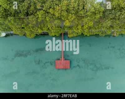 Ein roter Pier an einem grünen, krytalen, klaren See. Es gibt Bäume an der Küste. Stockfoto