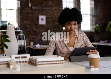 Birassische Architektin mit Tablet am Schreibtisch mit Baumodell im Büro Stockfoto