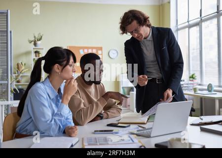 Ein vielseitiges junges Business-Team aus drei Mitarbeitern, die an einem Projekt im Büro zusammenarbeiten und Daten diskutieren Stockfoto