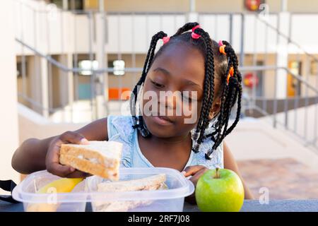 afroamerikanisches Schulmädchen am Tisch und gesundes Mittagessen mit Sandwich in der Grundschule Stockfoto